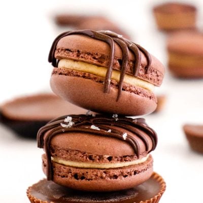 Two peanut butter chocolate macarons stacked on top of a peanut butter cup on a white table.