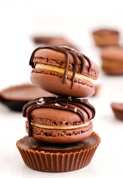 Two peanut butter chocolate macarons stacked on top of a peanut butter cup on a white table.
