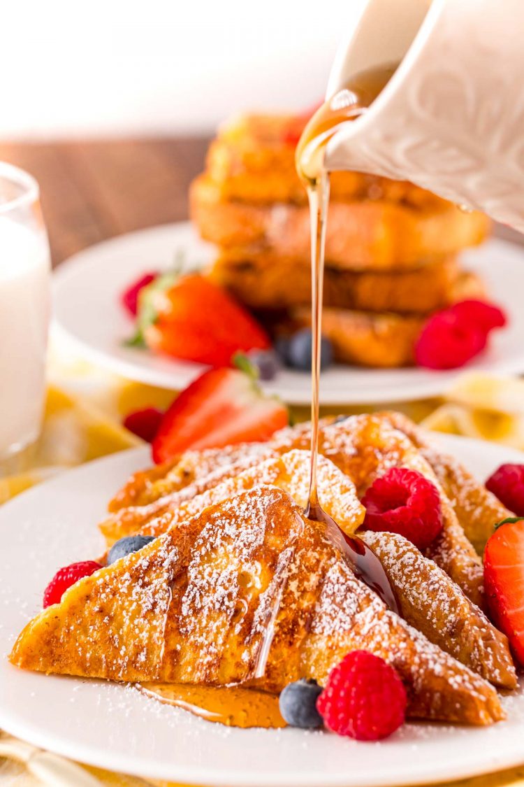Maple syrup being poured over the top of a plate of French toast with berries.