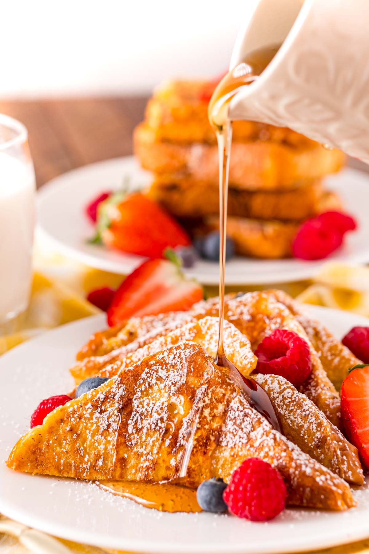 Maple syrup being poured over the top of a plate of French toast with berries.