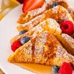 Close up photo of french toast on a white plate with berries and syrup.
