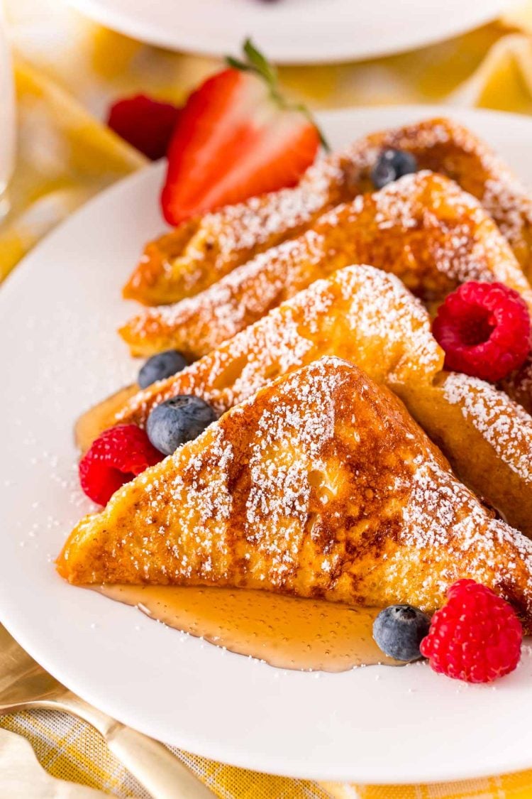 Close up photo of french toast on a white plate with berries and syrup.