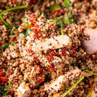 A serving spoon scooping out a serving of Greek Chicken Quinoa from a pan.