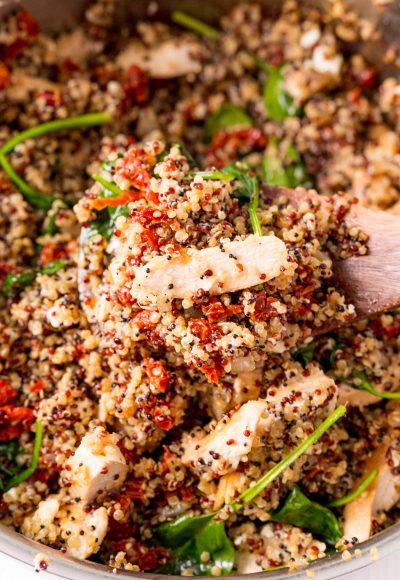 A serving spoon scooping out a serving of Greek Chicken Quinoa from a pan.