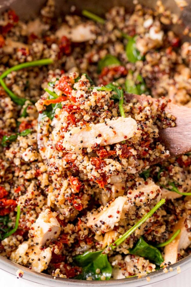 A serving spoon scooping out a serving of Greek Chicken Quinoa from a pan.