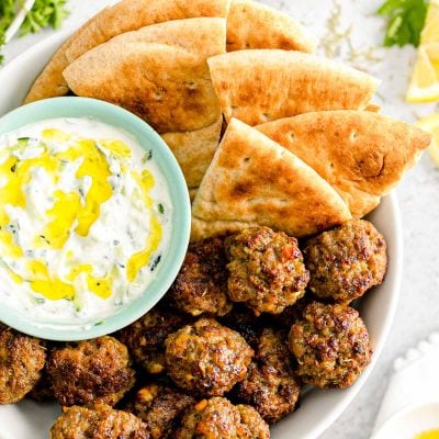 Overhead close up photo of Greek meatballs in a bowl with pita bread and tzatziki sauce.