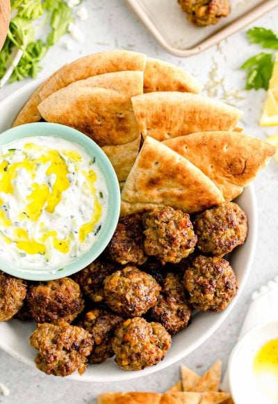 Overhead close up photo of Greek meatballs in a bowl with pita bread and tzatziki sauce.