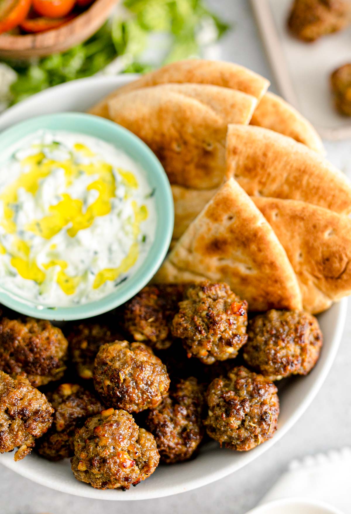 Close up photo of Greek meatballs in a bowl with tzatziki sauce and pita bread.