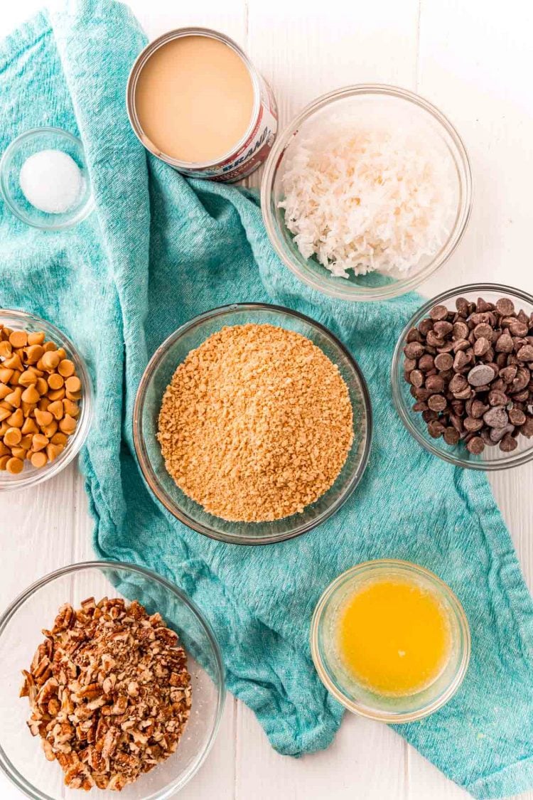 Ingredients to make hello dolly or seven layer bars on a white table with a blue napkin.