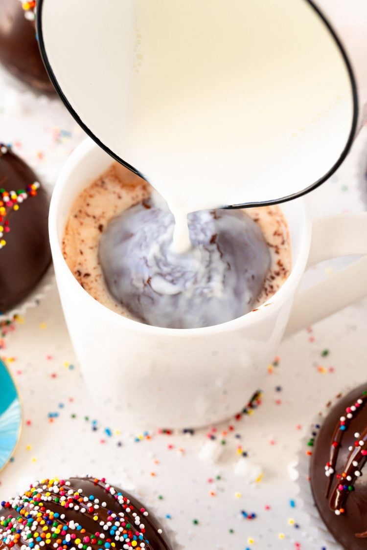 Milk being poured over a hot chocolate bomb in a white mug.