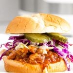 Close up photo of a bbq chicken sandwich with coleslaw and pickles with an instant pot in the background.