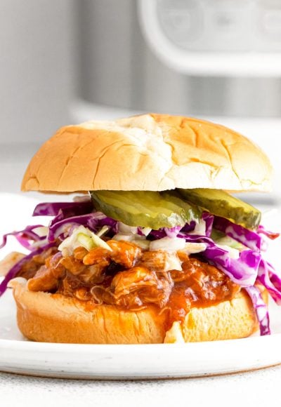 Close up photo of a bbq chicken sandwich with coleslaw and pickles with an instant pot in the background.