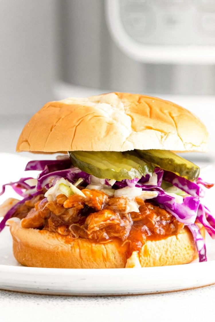 Close up photo of a bbq chicken sandwich with coleslaw and pickles with an instant pot in the background.