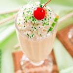 Close up photo of a milkshake glass filled with a Bailey's milkshake and topped with whipped cream and a cherry on a green napkin.