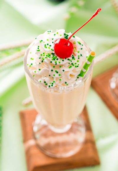 Close up photo of a milkshake glass filled with a Bailey's milkshake and topped with whipped cream and a cherry on a green napkin.