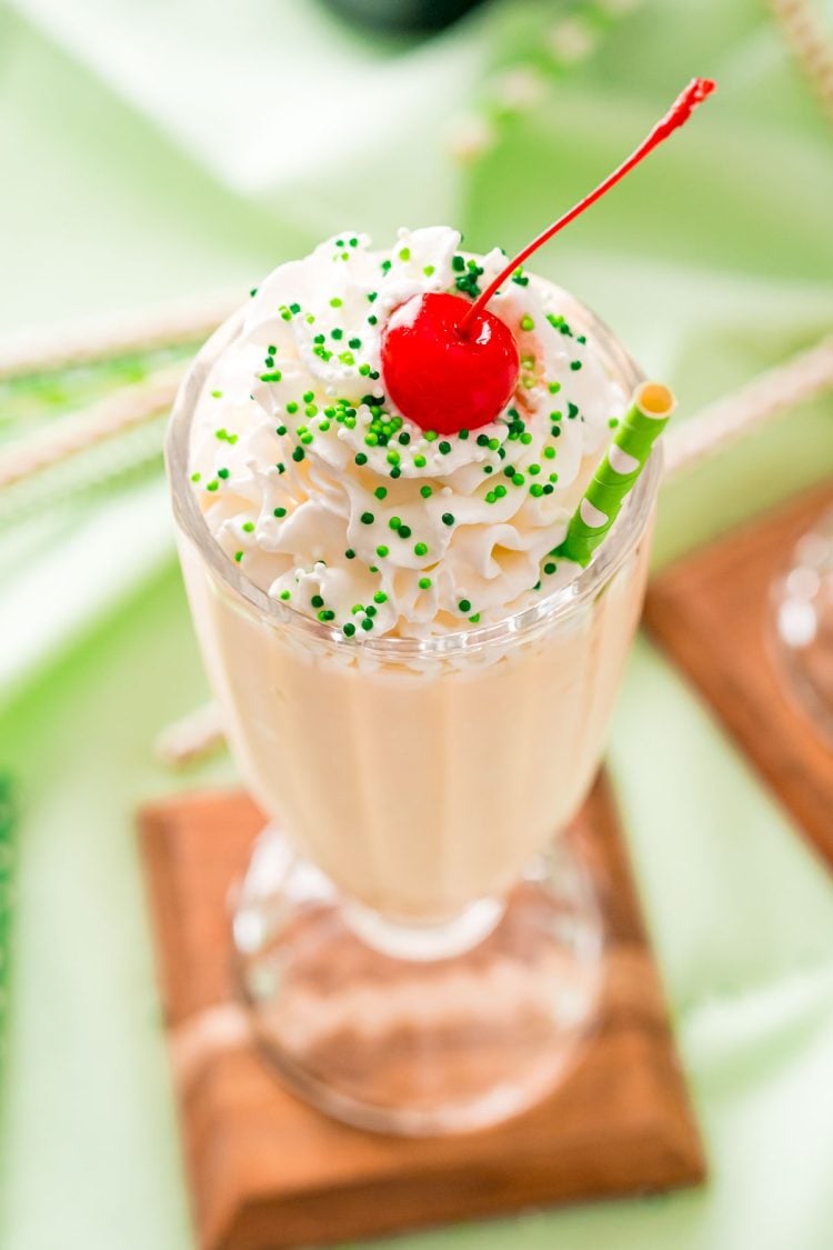 Close up photo of a milkshake glass filled with a Bailey's milkshake and topped with whipped cream and a cherry on a green napkin.