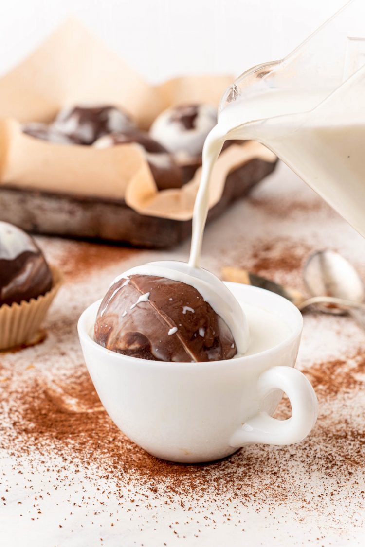 Milk being poured into a white mug with a hot cocoa bomb.