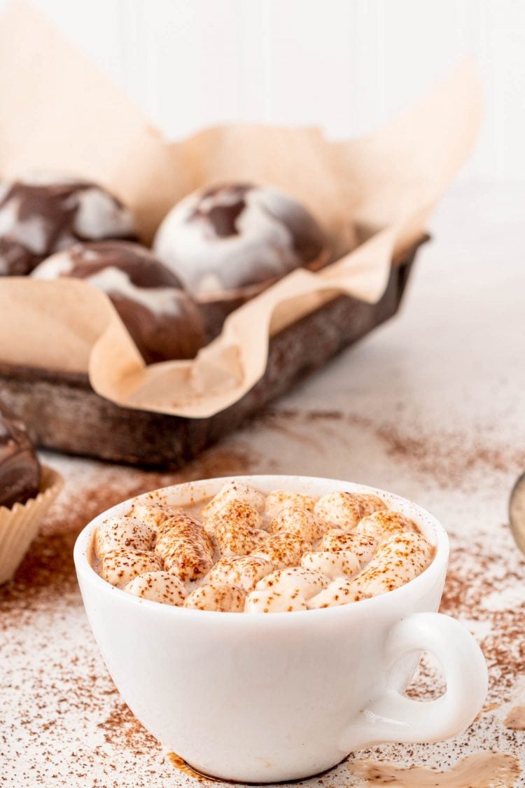 A mug of hot chocolate with hot chocolate bombs in the background.