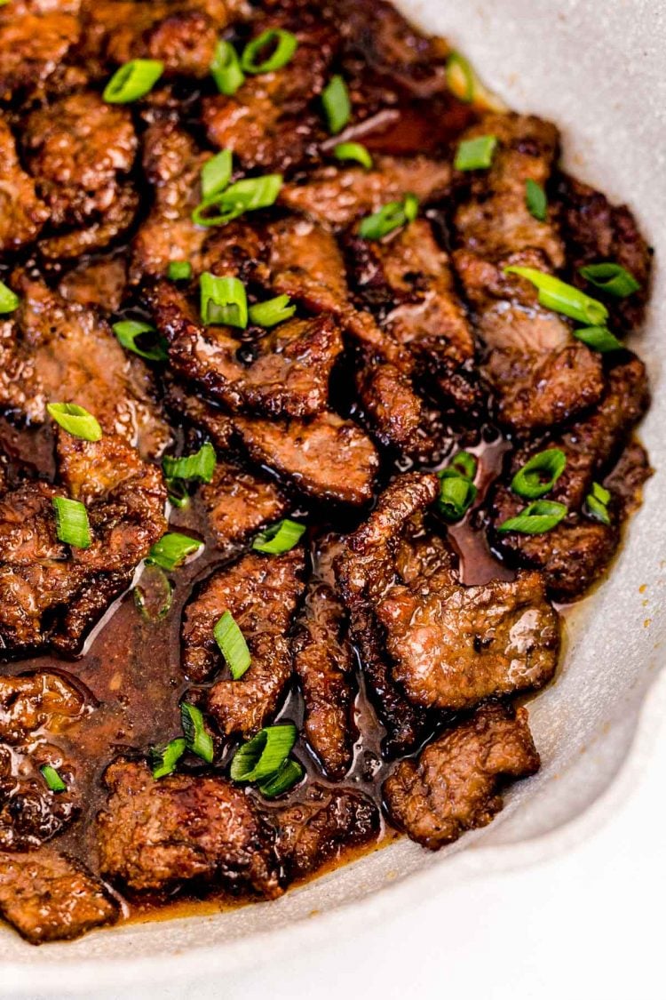 Close up photo of Mongolian beef in a pan garnished with scallions. 