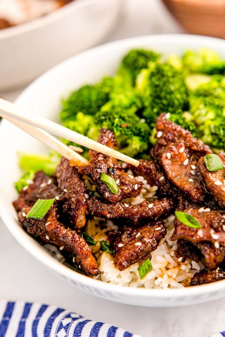 Chop sticks taking a piece of Mongolian beef out of a bowl.