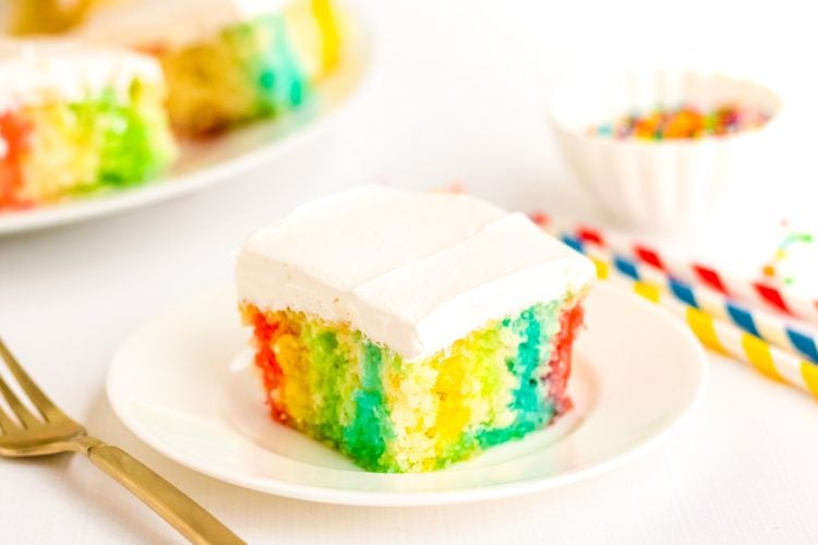 Close up photo of a slice of rainbow cake on a white plate.