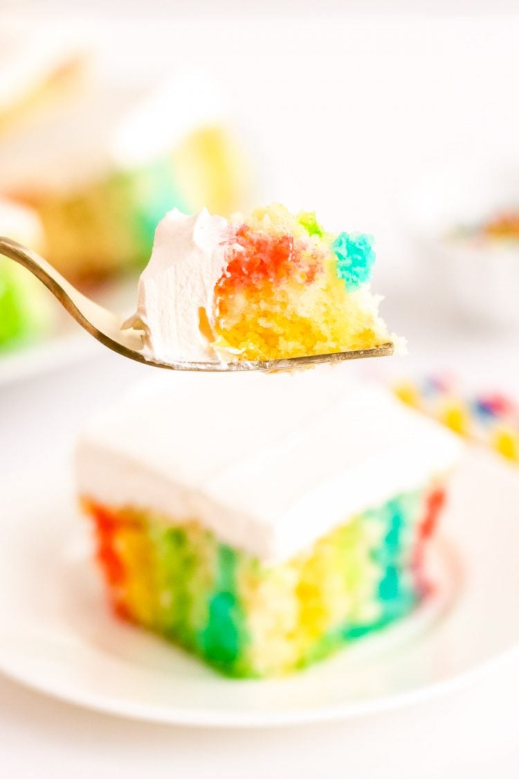 A bite of rainbow cake on a fork being held to the camera.