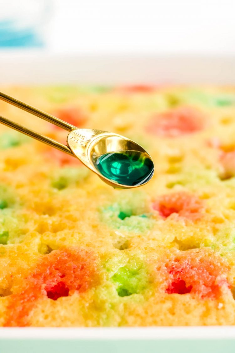 Close up photo of a teaspoon pouring jello over holes in a poke cake.