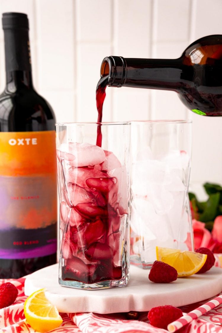 Red wine being poured into a tall glass with ice.