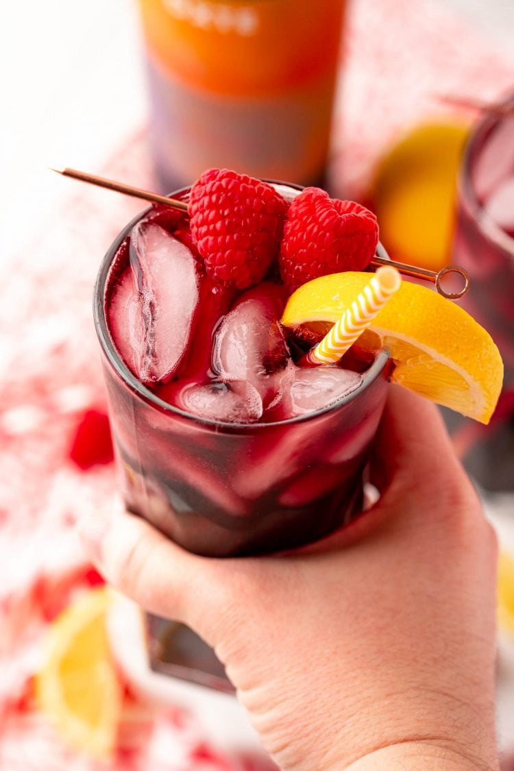 A woman's hand holding a red wine spritzer to the camera.