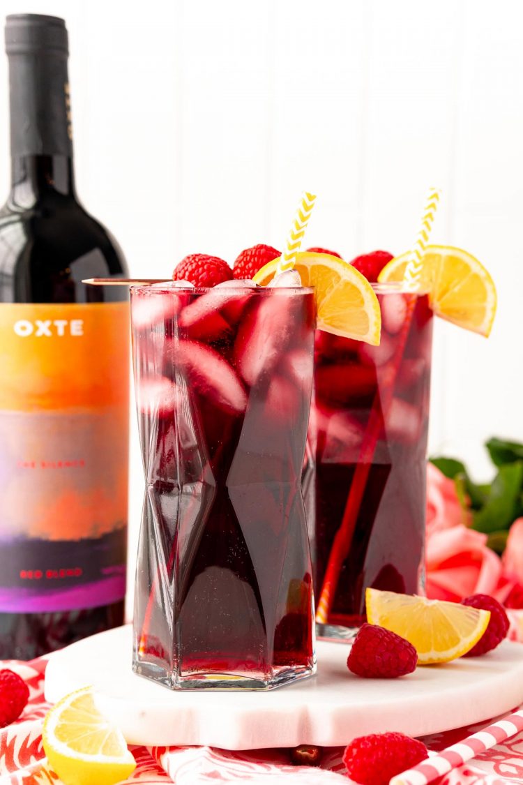 Straight on photo of two glasses filled with red wine spritzers on a marble tray with a bottle of red wine in the background.