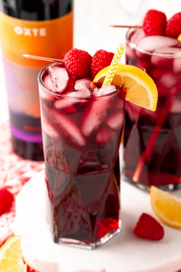 Close up photo of a red wine spritzer garnished with raspberries and lemon wedge.