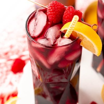 Close up photo of a red wine spritzer garnished with raspberry and lemon wedge.