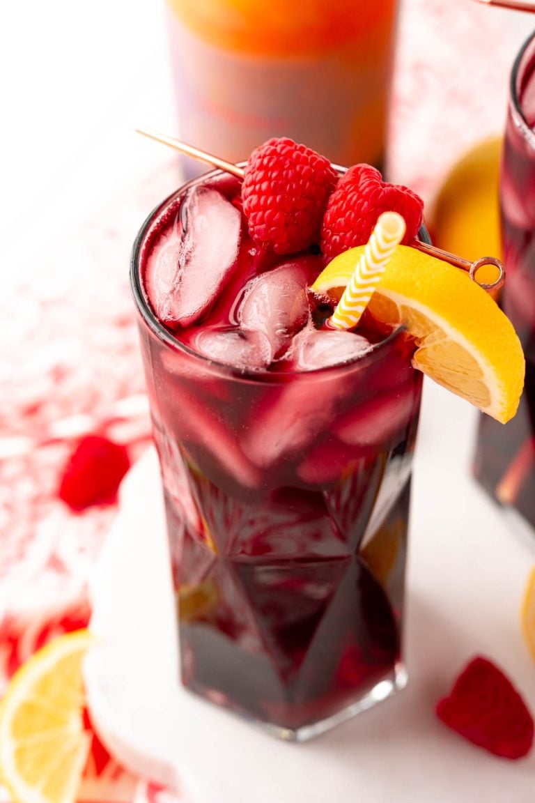 Close up photo of a red wine spritzer garnished with raspberry and lemon wedge.