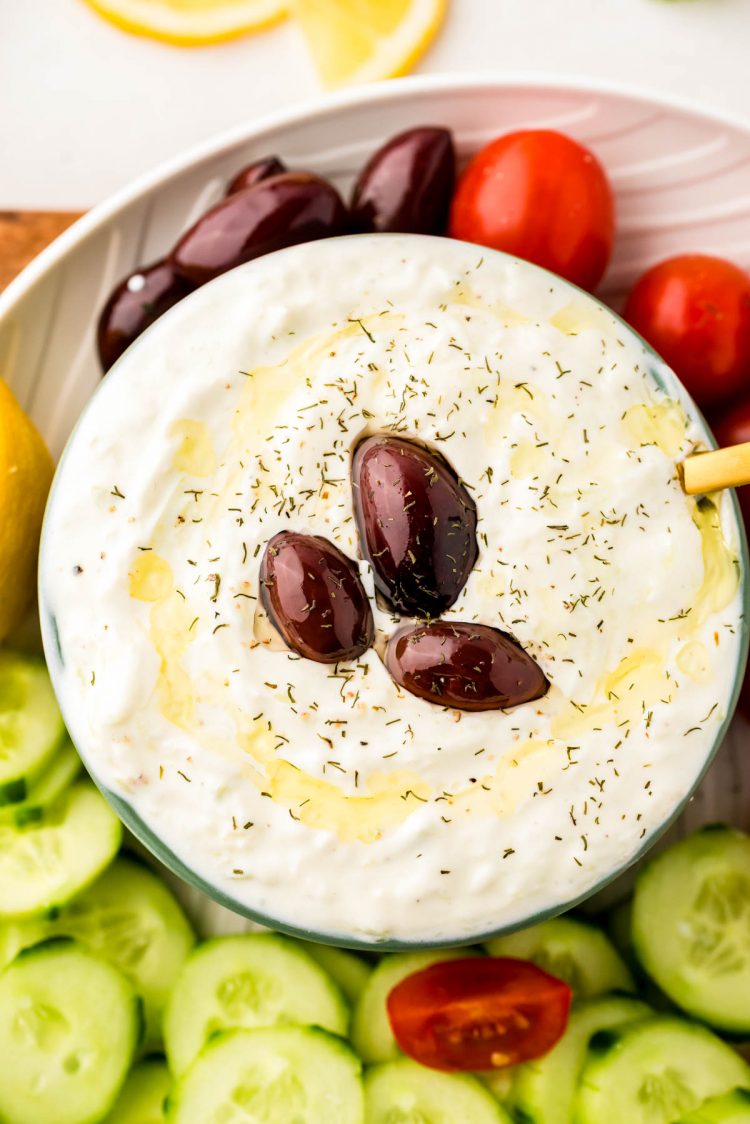 Overhead photo of a bowl of tzatziki sauce with veggies around it.