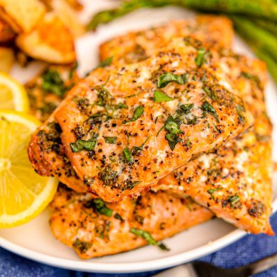 Close up photo of air fryer salmon filets on a white plate with lemon and asparagus in the background.