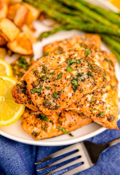 Close up photo of air fryer salmon filets on a white plate with lemon and asparagus in the background.