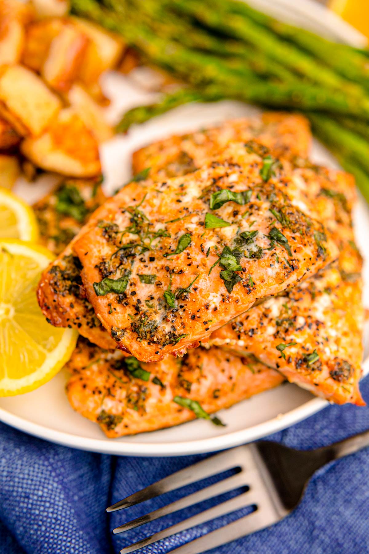 Close up photo of air fryer salmon filets on a white plate with lemon and asparagus in the background.