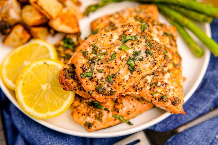 Close up photo of air fryer salmon filets on a white plate with lemon and asparagus in the background.