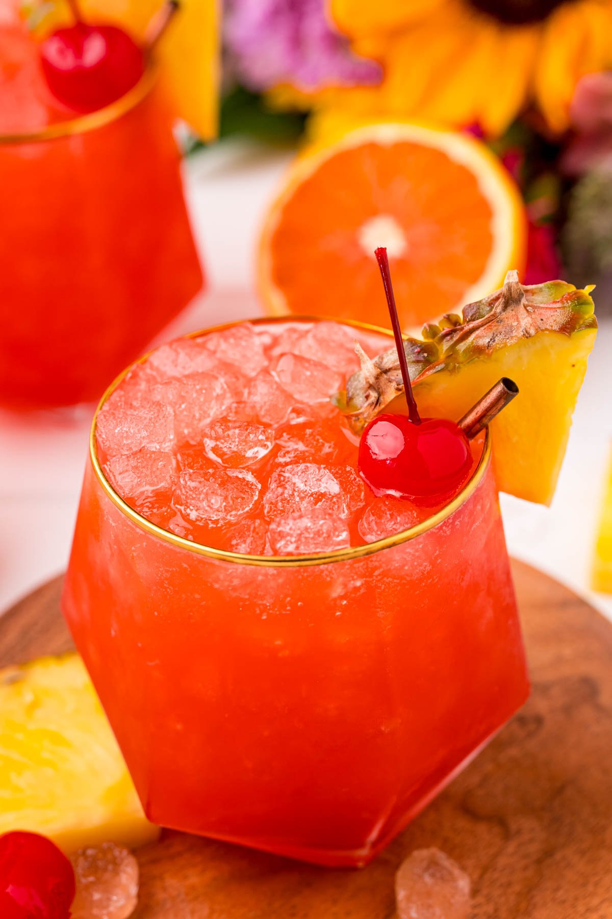 Close up photo of a gold rimmed glass with a bahama mama in it garnished with a maraschino cherry and a pineapple wedge.