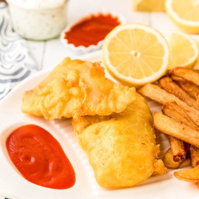 Pieces of fried fish on a white platter with fries and ketchup and lemon.