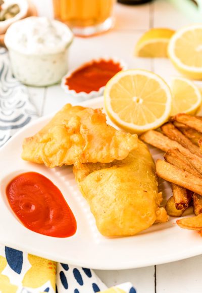 Pieces of fried fish on a white platter with fries and ketchup and lemon.