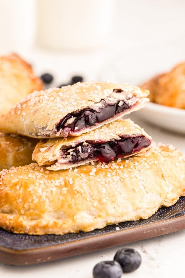 Photo of blueberry hand pies on a tray with a pie on top that's been split in half.