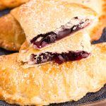 Close up photo of blueberry hand pies on a blue platter with one pie on top broken in half.