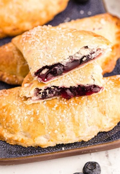 Close up photo of blueberry hand pies on a blue platter with one pie on top broken in half.