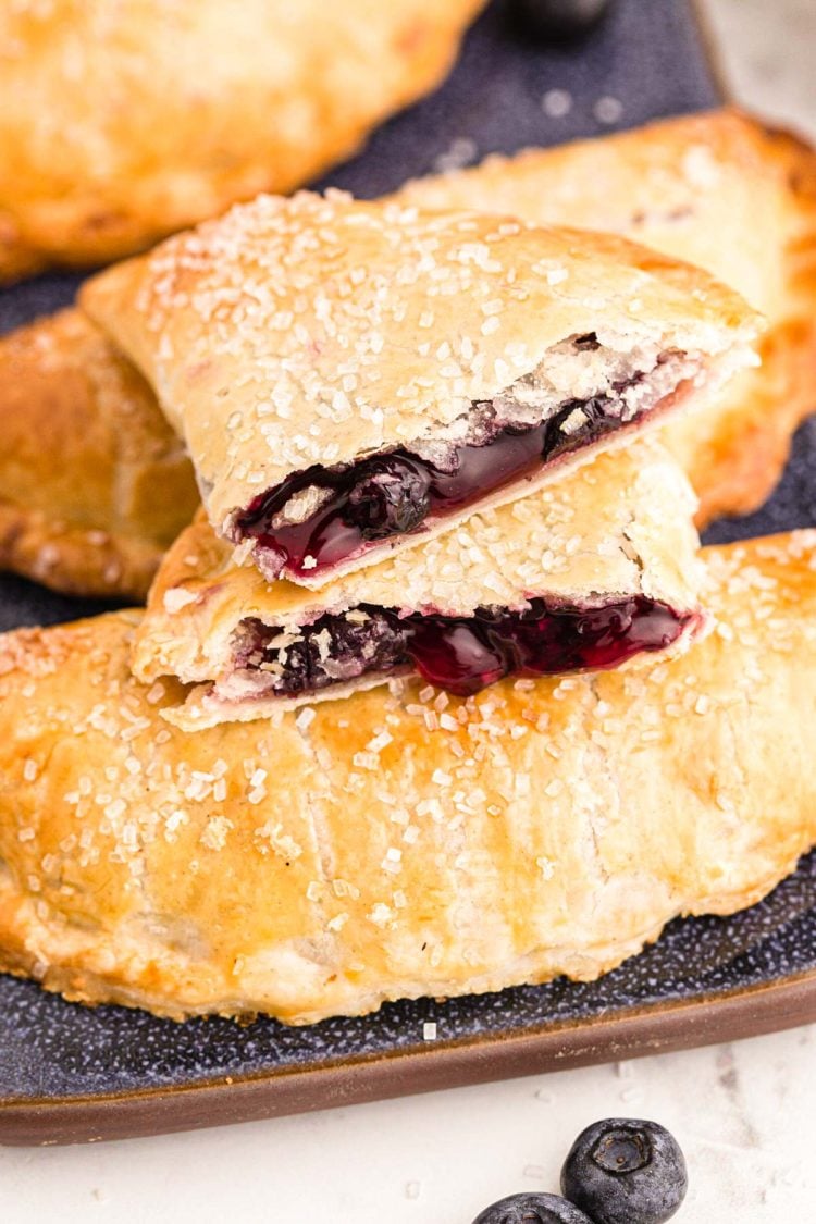 Close up photo of blueberry hand pies on a blue platter with one pie on top broken in half.