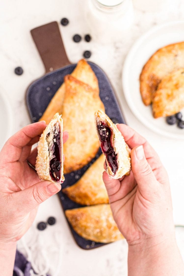 A woman's hands holding a blueberry hand pie that's been split in half.