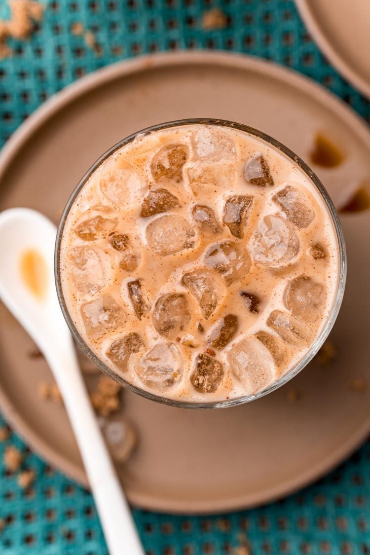 Close up photo of a brown sugar oatmilk shaken espresso on a brown plate with cinnamon sticks and brown sugar.