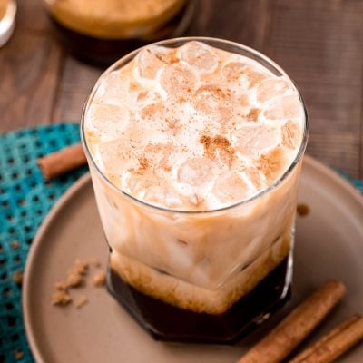 Close up photo of a brown sugar oatmilk shaken espresso on a brown plate with cinnamon sticks and brown sugar.