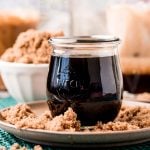 Close up photo of a jar of brown sugar simple syrup on a brown plate with brown sugar all around it.