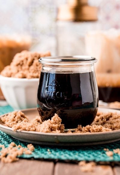 Close up photo of a jar of brown sugar simple syrup on a brown plate with brown sugar all around it.